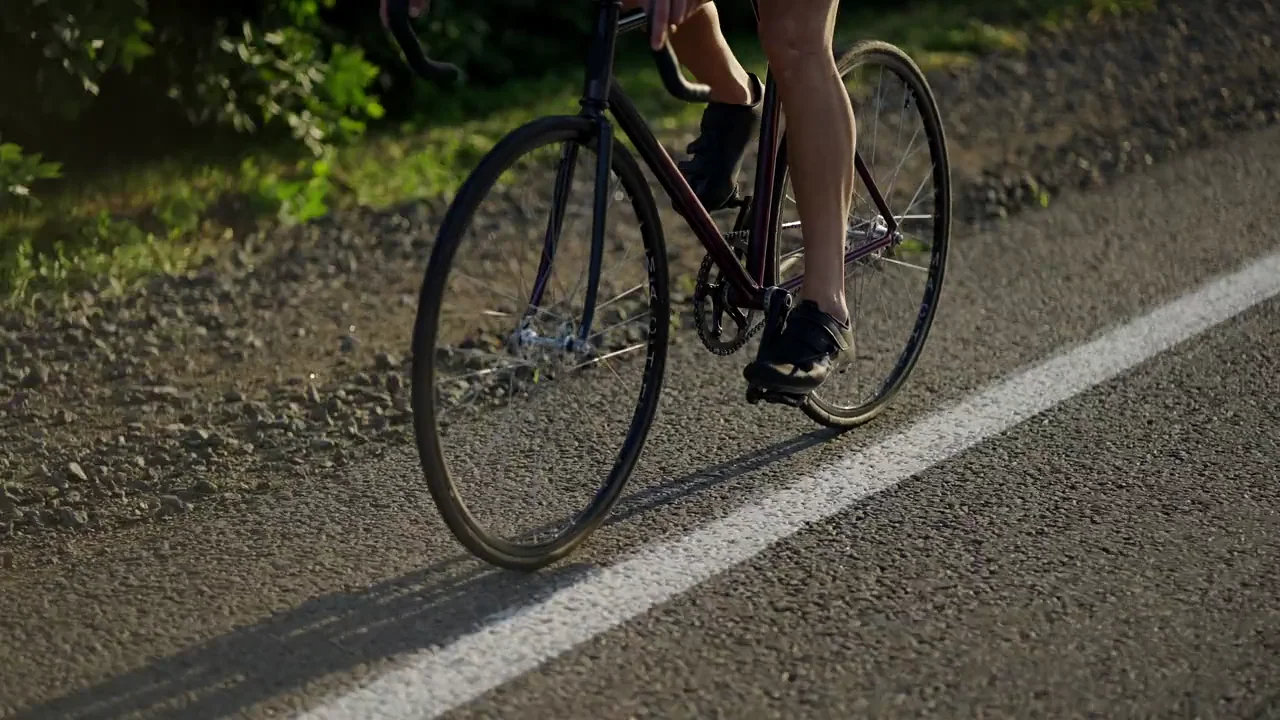 A cyclist riding along a sunlit road, seen close to the wheels